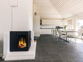 Una cocina moderna con armarios blancos, una chimenea con fuego a la vista y un comedor con sillas y mesa blancos.