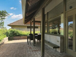A covered patio area with a table and chairs, a brick pathway, and a view of a house with a tiled roof.