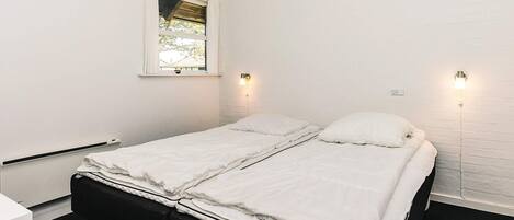 Une chambre avec un lit simple, du linge de lit blanc, une fenêtre et deux lampes fixées au mur.