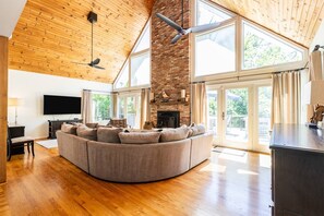A spacious living area with a large curved sofa, a fireplace, and a television. - Quiet Woodland Lodge w Community Beach Access & Large Private Deck (Annapolis)