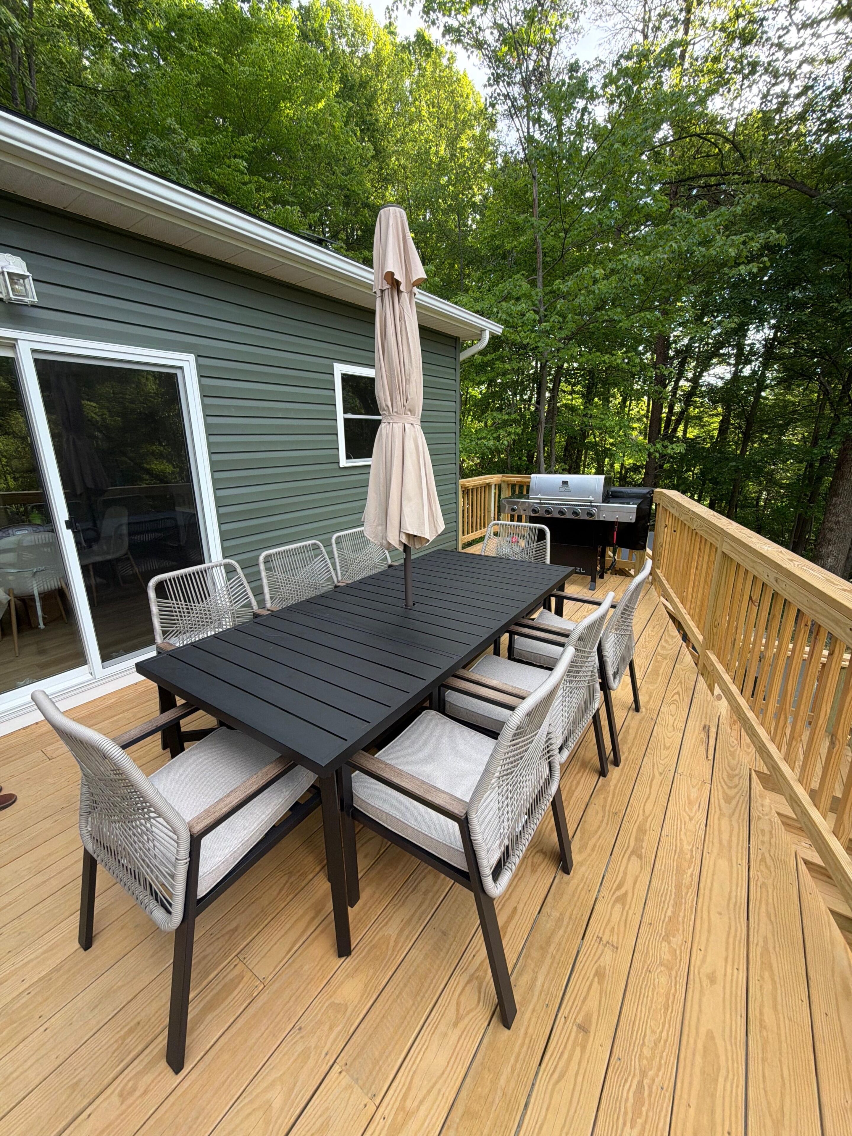 A deck with a table and chairs, a grill, and a covered umbrella.