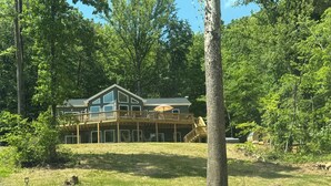A two-story cabin with a deck, surrounded by trees.