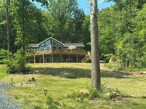 A two-story cabin with a deck, surrounded by trees. - Shenandoah Chalet - Hot Tub, Sauna, Movie theater, Game Room, EV charger, Hiking (Bentonville)