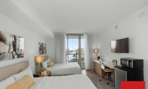 Ein Hotelzimmer mit zwei Betten, einem Schreibtisch, einem Fernseher und Blick auf eine Stadtlandschaft.