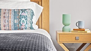 Un letto rifatto con cuscini decorati, un comodino con un vaso verde e una tazza, e un libro intitolato 'ISOBARS HOSPITAL'.