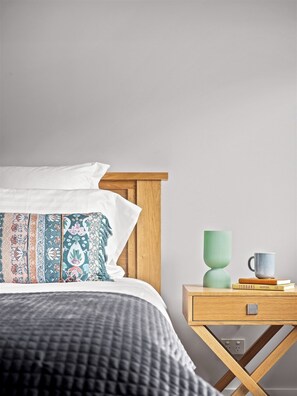 A neatly made bed with patterned pillows, a bedside table with a green vase and a mug, and a book titled 'ISOBARS HOSPITAL'. - Stunning two story home in town centre (Margaret River)