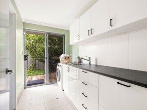 A modern kitchen with white cabinets, a black countertop, and a sliding glass door leading to a garden. - Stunning two story home in town centre (Margaret River)