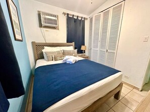A bedroom with a bed, a nightstand, a lamp, a wardrobe, and an air conditioning unit. - Villa 10 Villas Flamenco frente al mar (Culebra)
