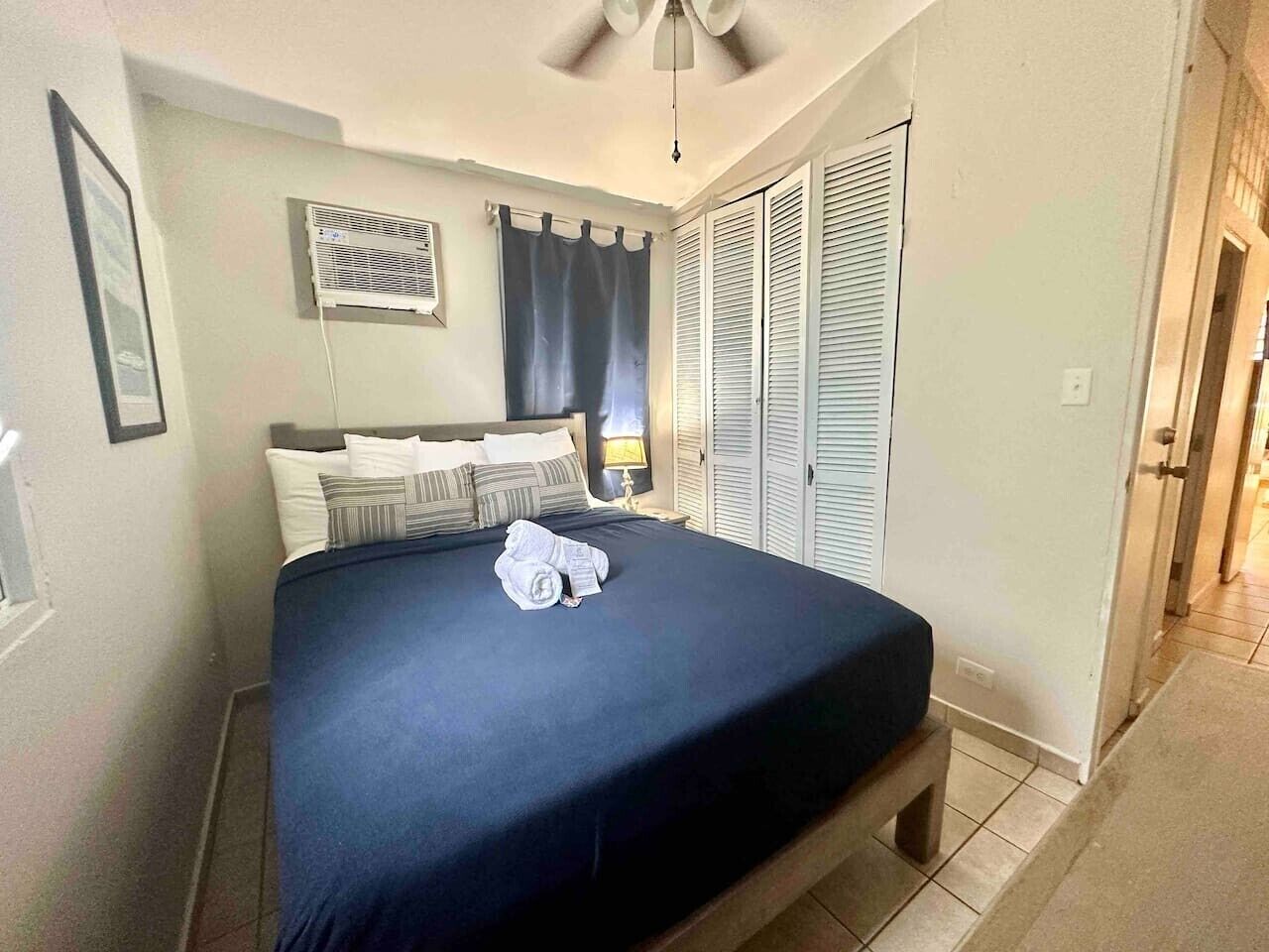 A hotel room with a bed, a ceiling fan, a window with curtains, and a door with a view.