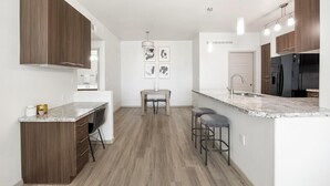 Una cucina moderna con mobili in legno, un piano di lavoro in marmo, un'area pranzo con tavolo e sedie e un frigorifero.
