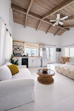A spacious living area with a kitchen, white furniture, and a ceiling fan.