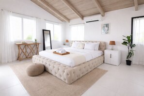 A bedroom with a large bed, bedside tables, a desk, a potted plant, and a ceiling fan.