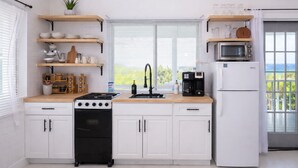A kitchen with white cabinets, a stove, a sink, and a microwave. - Cozy 2bdrm private home/Cayman Brac W/ AC, gym, WiFi & outdoor tub (Cayman Islands)
