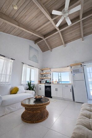 A spacious living area with a ceiling fan, a dining table, a kitchen with white cabinets, and a view of the sea.