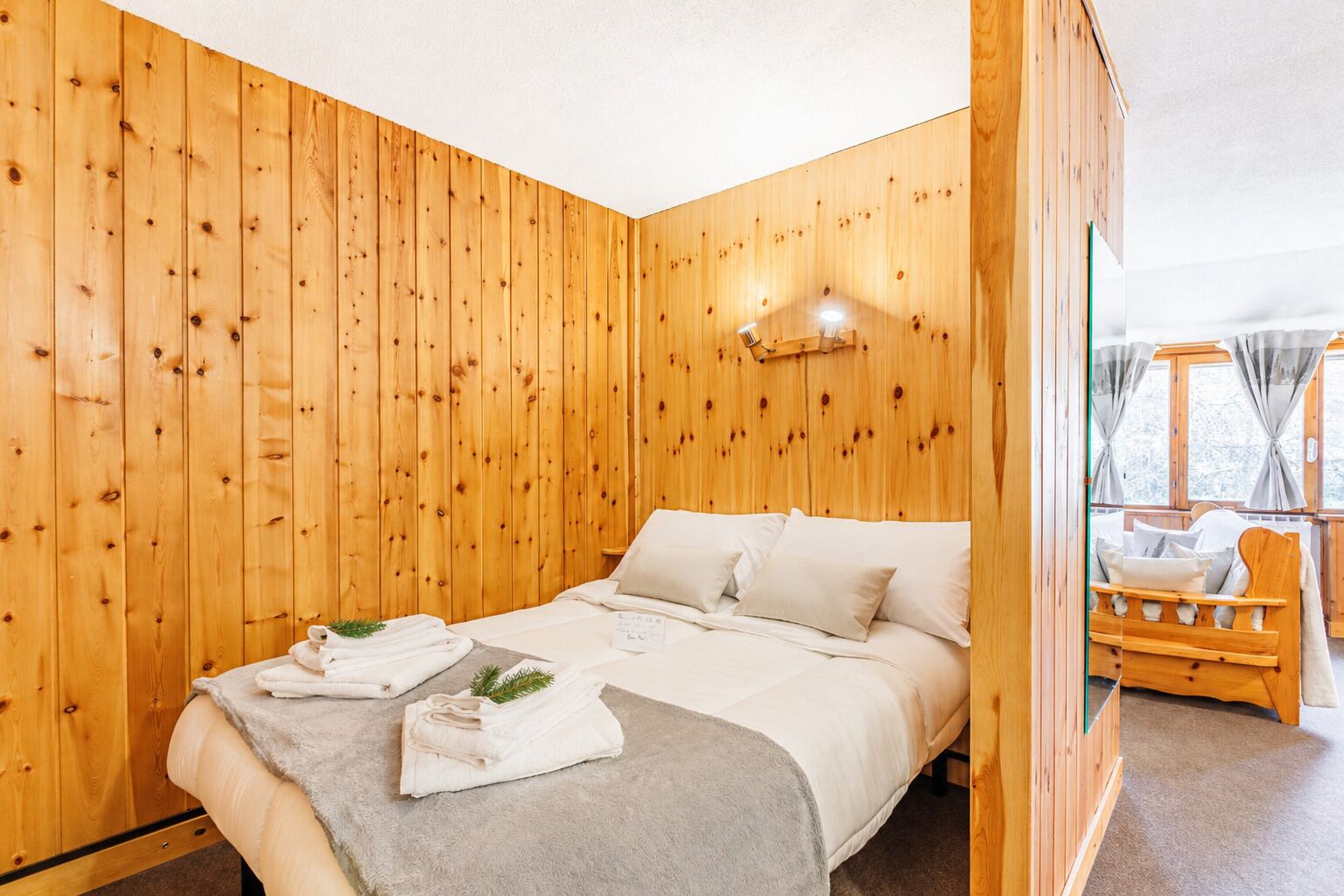 A wooden-paneled room with a bed, towels, and a small table.