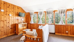 A cozy room with wooden walls, a bed, a TV, and large windows with curtains. - Petit Chalet Pila (Pila)