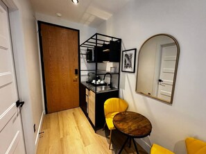 A compact kitchen with a sink, a dining area with a round table and two chairs, a wooden door, and a mirror on the wall. - Boutique Old Montreal Suite-1B (Montreal)