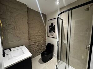 Ein Badezimmer mit Waschbecken in Weiß, Toilette in Schwarz und einer Duschkabine aus Glas.