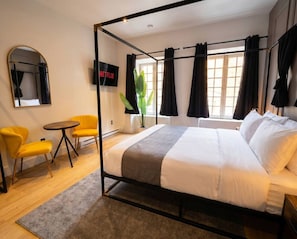 A modern hotel room with a four-poster bed, a round table, two yellow chairs, a large mirror, and a Netflix TV. - Boutique Old Montreal Suite-1B (Montreal)