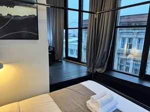 Ein Hotelzimmer mit Bett, einem Vorhangfenster, einem Bild an der Wand und Blick auf ein Gebäude.
