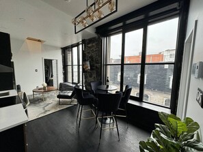 Ein modernes Interieur mit Essbereich, großen Fenstern und Blick auf umliegende Gebäude.