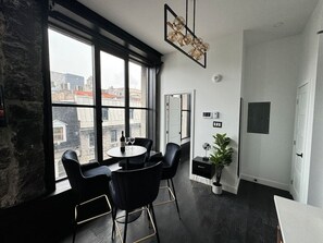 Ein modernes Zimmer mit einem großen Fenster, einem runden Tisch mit Stühlen, einer Topfpflanze und einer Tür.