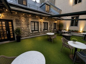An outdoor patio with round tables and chairs, stone walls, and string lights. - Boutique Old Montreal Suite-1C (Montreal)