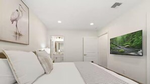 A bedroom with a bed, a television, a framed picture, and a mirror.