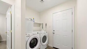 A laundry room with two front-loading washing machines, a drying rack, and a white door.