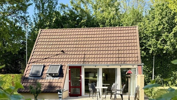 Ein kleines Haus mit geneigtem Dach, Glastür und Terrasse mit Gartenmöbeln.