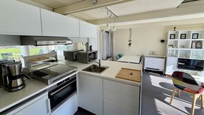 Eine kleine Küche mit Herd, Mikrowelle und Spüle, ein Essbereich mit einem Stuhl und ein Bücherregal mit gerahmten Bildern.