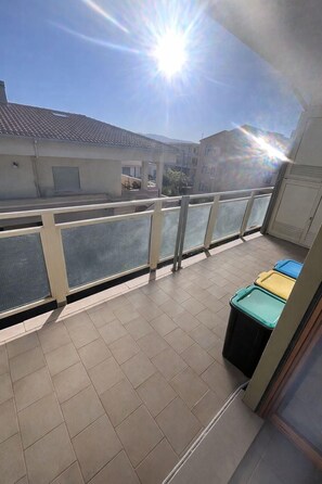 A balcony with a view of buildings, a tiled floor, and a trash bin. - Valledoria House - Two Bedroom Apartment, Sleeps 4 (Valledoria)