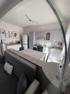 A compact living space with a kitchenette, a dining area, and a sofa with a decorative pillow. - Valledoria House - Two Bedroom Apartment, Sleeps 4 (Valledoria)