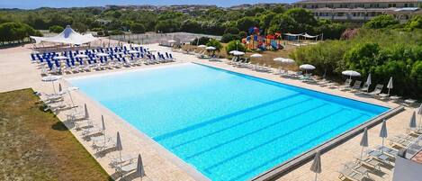A large rectangular swimming pool with clear blue water, surrounded by lounge chairs and umbrellas.