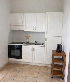A compact kitchen with white cabinets, a black oven, a small wooden table, and a coffee maker. - Villa Aura - Two Bedroom Apartment, Sleeps 6 (Pirotto Li Frati)