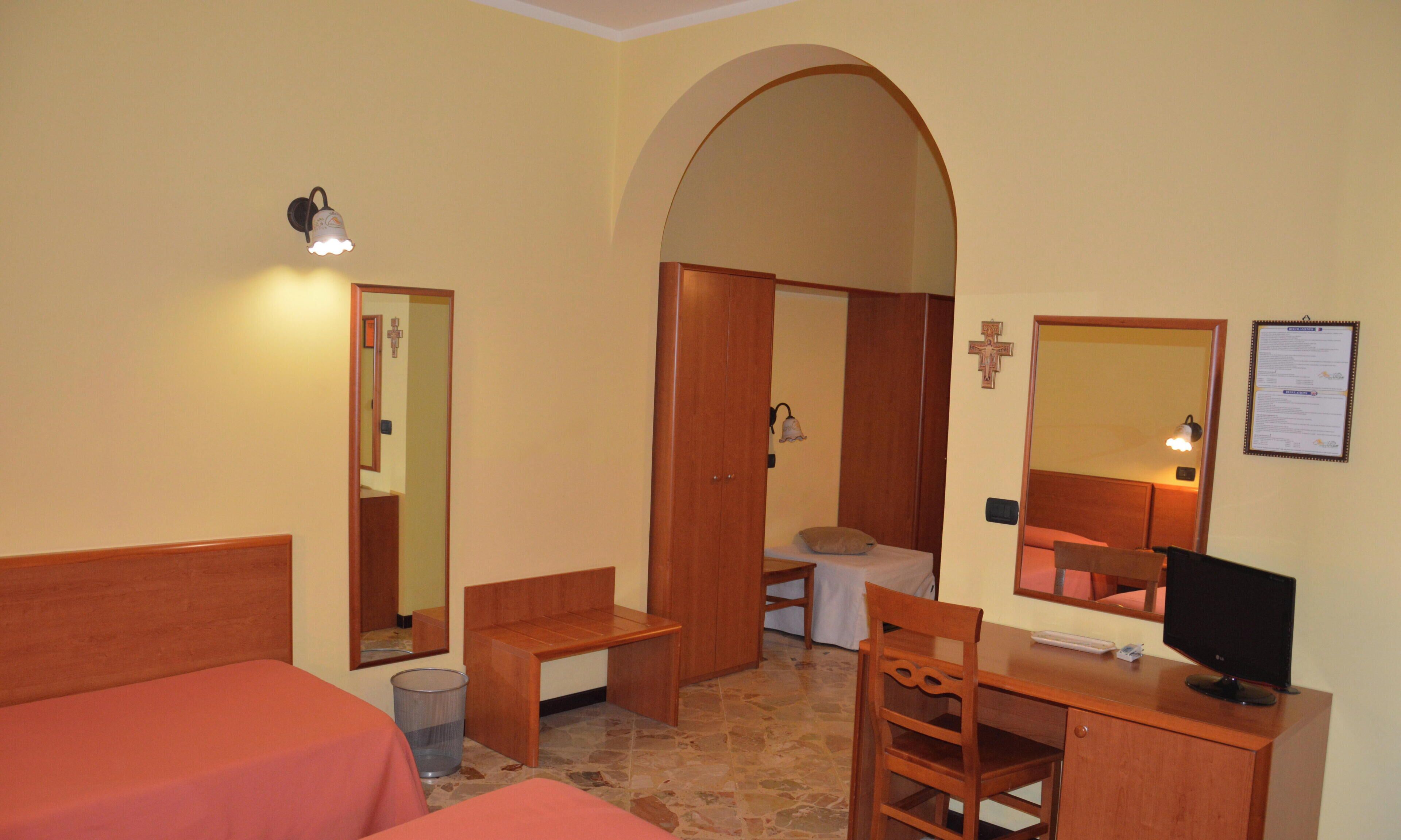 Ein Hotelzimmer mit einem Bett, einem Schreibtisch, einem Stuhl, einem kleinen Tisch, einem Mülleimer und einem Spiegel.