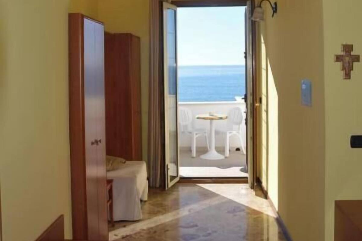A corridor with an arched doorway leading to a balcony with a view of the sea.