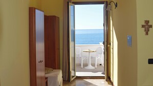 A hallway leading to a balcony with a view of the sea, a cross on the wall, and a small table with chairs. - B&B Mare e Sole Villa Urso (Avola)