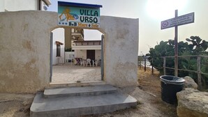 A villa entrance with a sign, steps leading to a building, outdoor seating, and a cactus plant. - B&B Mare e Sole Villa Urso (Avola)