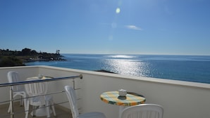 A balcony with white chairs and a small table, overlooking a coastal view with the sea and a distant shoreline. - B&B Mare e Sole Villa Urso (Avola)