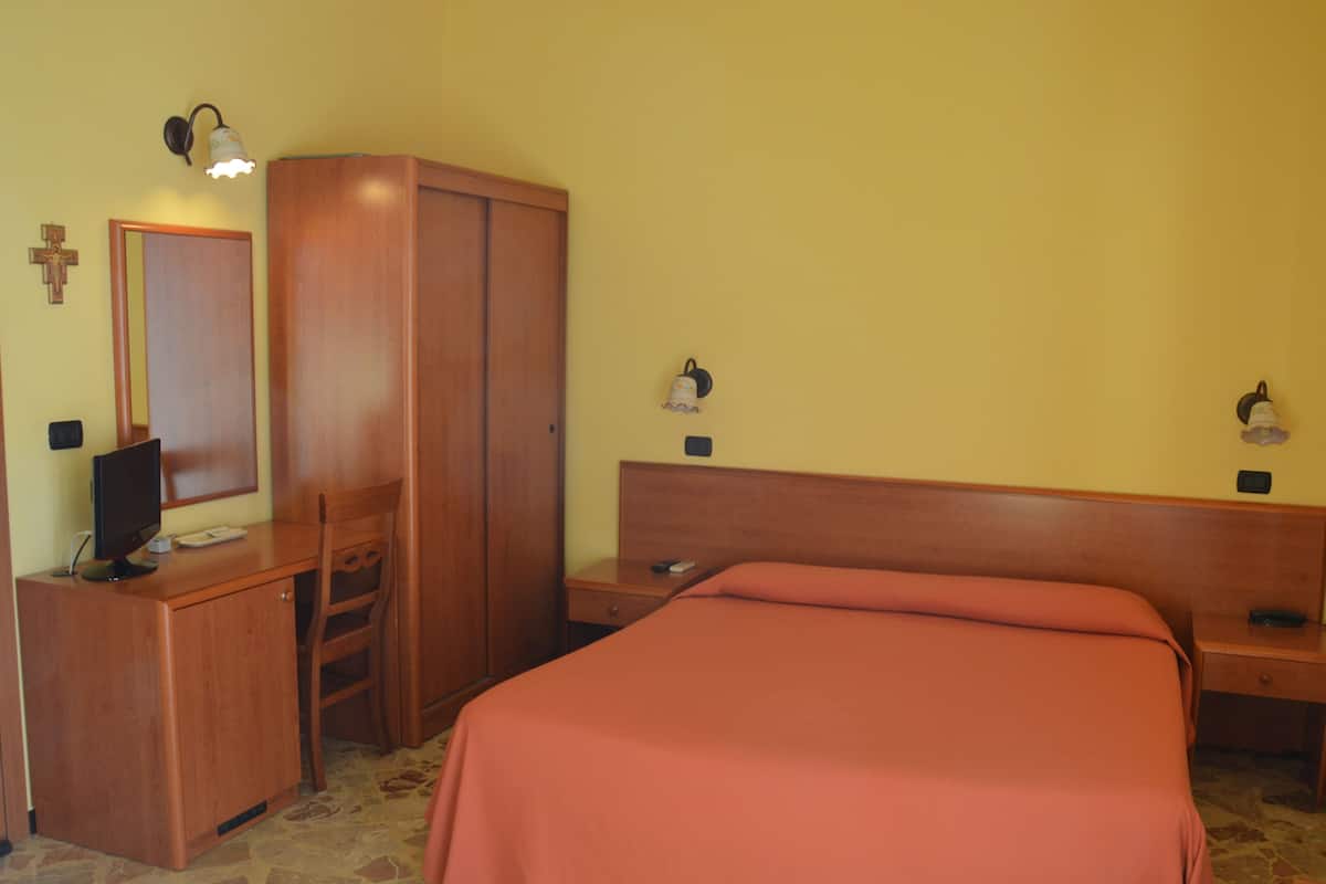 A bedroom with a bed, a wooden wardrobe, a desk with a computer, and two bedside lamps.