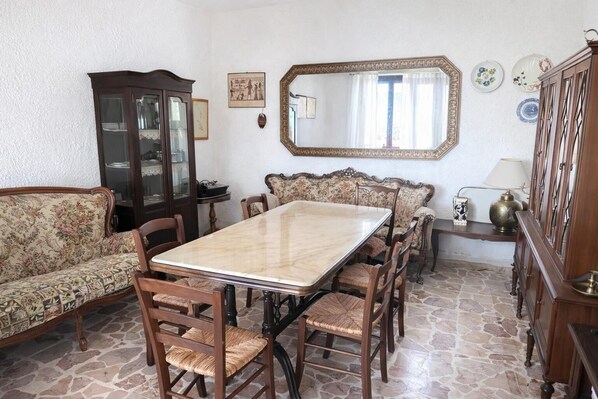 Un coin repas comprenant une table en marbre, des chaises en bois, un canapé à motifs floraux, un meuble et un miroir.