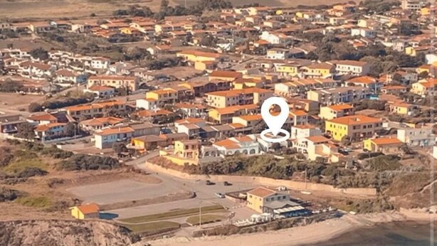 Vista aérea de un pueblo costero con edificios, una playa y un puerto deportivo.