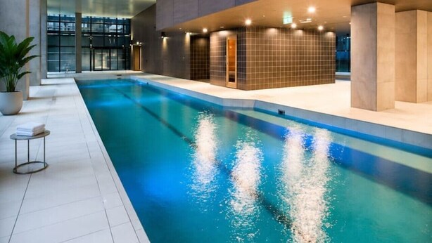 Una piscina interior con suelo de baldosas, una planta en maceta y una pequeña mesa.