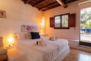 A bedroom with a large bed, bedside tables, a window, and a view of the outside. - New! Villa Ses Cases Altes de Arabí (Ibiza)
