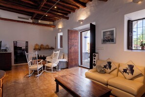 A cozy living room with a wooden ceiling, a sofa, a rocking chair, and a dining table. - New! Villa Ses Cases Altes de Arabí (Ibiza)
