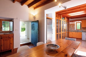 A wooden dining table with chairs, a bowl, and a kitchen with wooden cabinets and a refrigerator. - New! Villa Ses Cases Altes de Arabí (Ibiza)