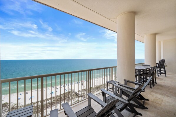 Un balcon avec vue sur la plage et l’océan, des sièges d’extérieur et une balustrade.