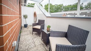 Ein Balkon mit Korbmöbeln, einer Topfpflanze und Blick auf Bäume.