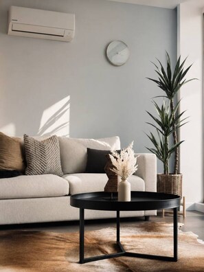 A modern living room with a sofa, a coffee table, a potted plant, and a wall-mounted clock. - Spacious 2BR City Views Retreat (Melbourne)